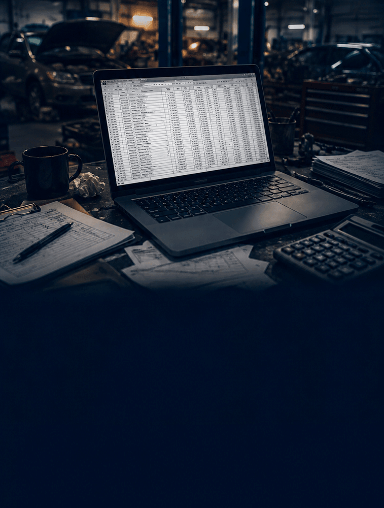 Planilha aberta em um notebook sobre a bancada de uma oficina de funilaria.